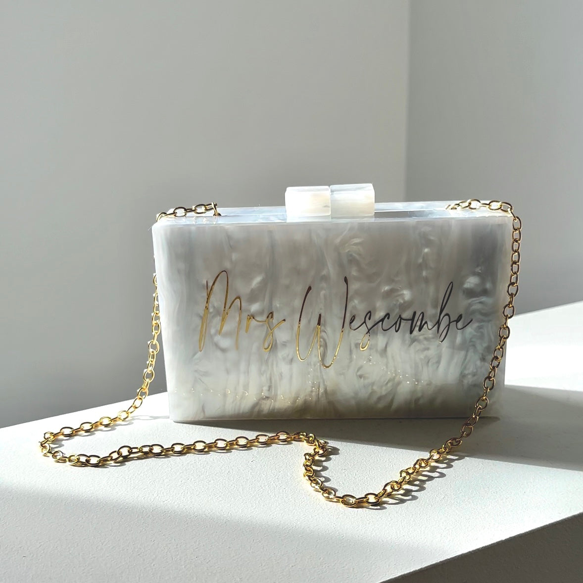 white acrylic marble look clutch with metallic gold writing of customers choice. gold chain attached whoch is detachable